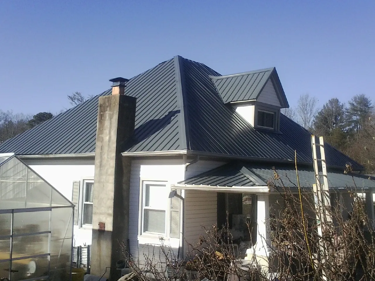 Dark blue standing seam metal roof on a white farmhouse with dormer — Slate & Tile Roof Repair by Roofing Brothers in Hayden