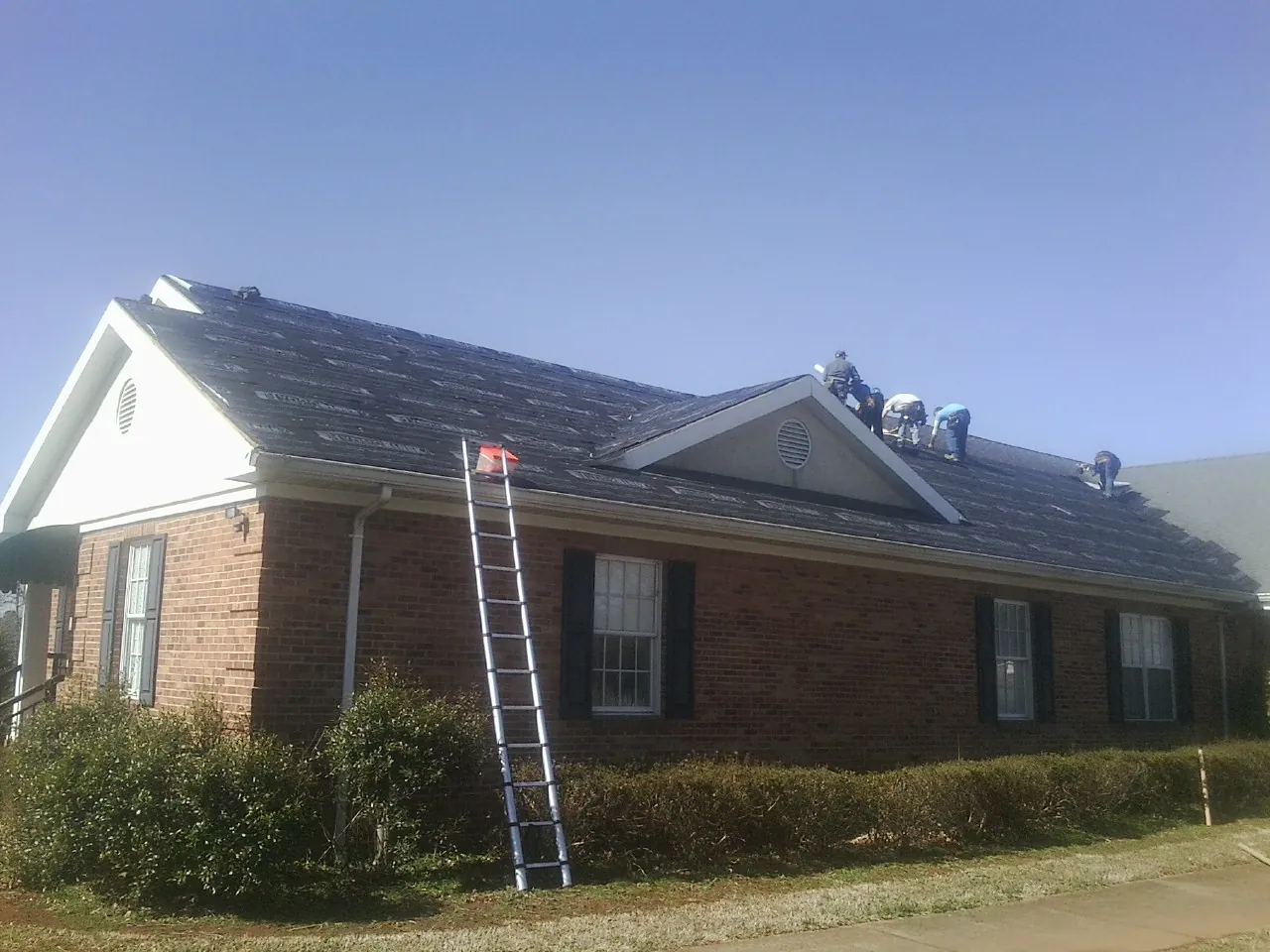 Crew tearing shingles off a brick ranch roof with a ladder set — Emergency Roof Repair work by our crew in Hayden