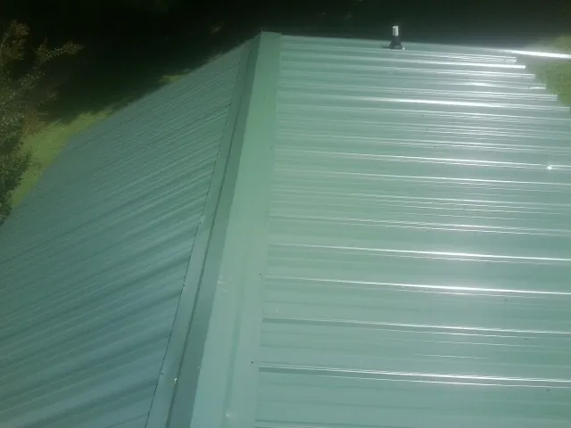 New green metal panels meeting at the ridge of a roof — Flat Roof Repair work by our crew in Hayden